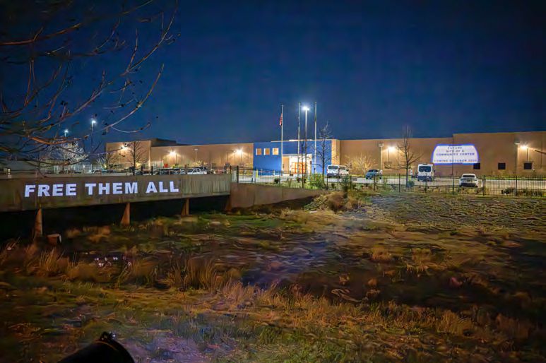 "FREE THEM ALL" projected on the side of the concrete bridge leading to the Aurora GEO Detention Center